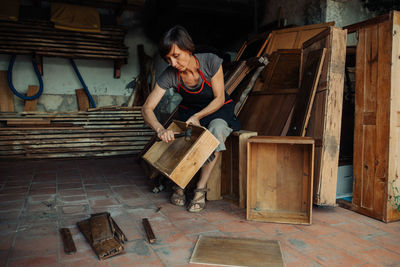 Female craftsperson breaking old wooden furniture for artistic reuse