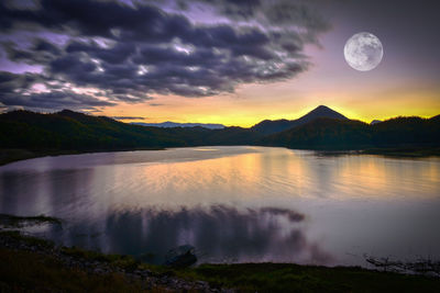 Scenic view of lake by mountains against sky at dusk