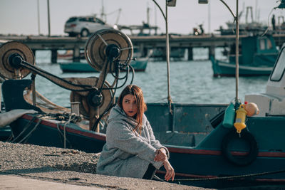 Woman looking away while sitting at harbor