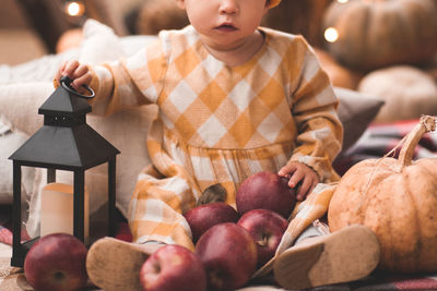 Baby girl 1-2 year old wearing yallow dress holding candle and fresh apples closeup. 