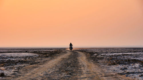 Person riding motorcycle on dirt road against sky during sunset