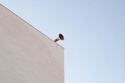 Low angle view of bird perching on building against clear sky