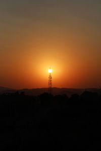 Silhouette communications tower on landscape against orange sky