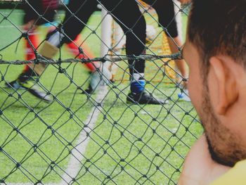 Close-up of man watching soccer through fence