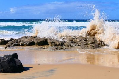 Waves splashing on rocks at beach against sky
