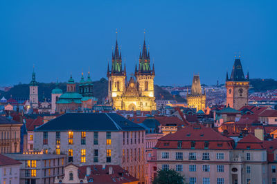 Illuminated buildings in city against blue sky