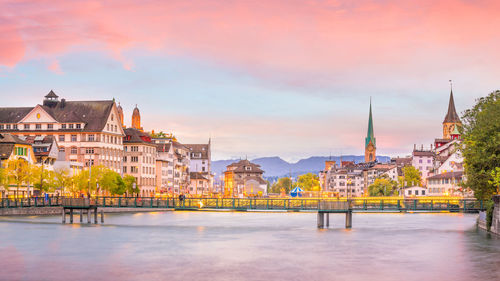 Bridge over river amidst buildings in city against sky