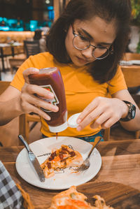 Woman holding sauce bottle over food on table at restaurant 