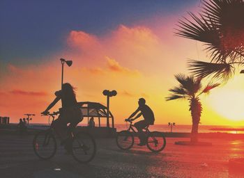Silhouette couple riding bicycles at sunset