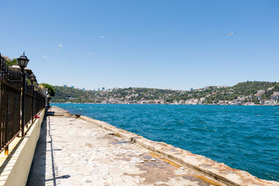 Empty footpath by sea against clear sky