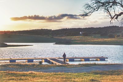 Man standing on pier against lake during sunset