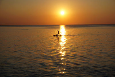 Silhouette man in calm sea at sunset