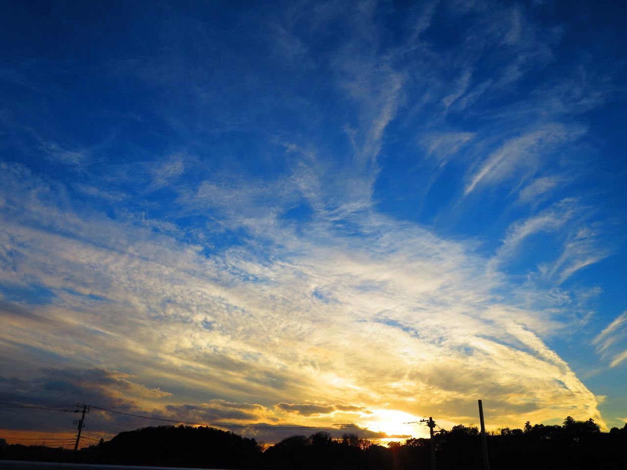 sunset, silhouette, sky, beauty in nature, tranquility, scenics, tranquil scene, low angle view, cloud - sky, nature, blue, idyllic, cloud, orange color, landscape, electricity pylon, sunlight, outdoors, no people, dramatic sky