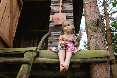 Full length of woman sitting on wood against tree