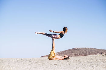 Man practicing acroyoga with female against clear sky