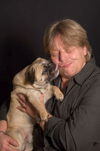 Pug licking mature man face against black background