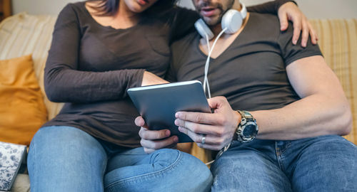 Low section of friends sitting on sofa at home