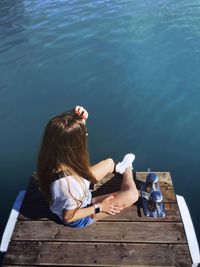 Rear view of woman sitting on pier over lake