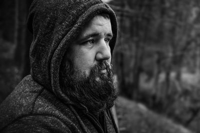 Thoughtful bearded man looking away while wearing hood outdoors