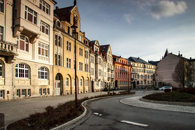 Road by buildings in city against sky