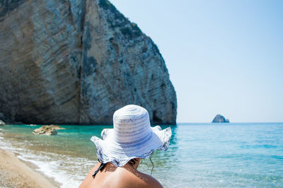 Woman sitting at beach while wearing sun hat on sunny day