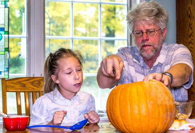 A little girl watches as grandpa makes delicate cuts in the operation of carving a jack o lantern
