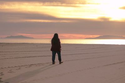 Rear view of woman walking at beach at sunset