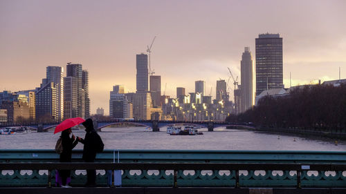 People on river amidst buildings in city against sky