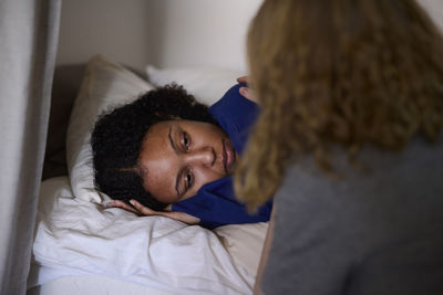 Young woman comforting friend lying in bed