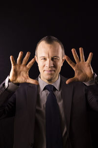 Portrait of businessman gesturing against black background