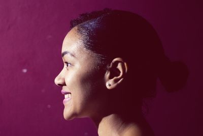 Profile view of smiling young woman looking away against red background