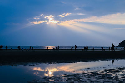 Silhouette people on beach against sky during sunset