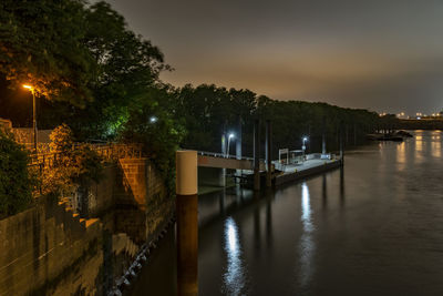 Illuminated city by river against sky at night