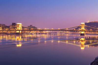 Illuminated bridge over river with city in background