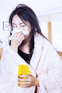 Woman blowing nose in facial tissue at home