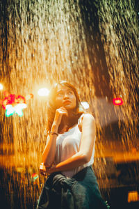 Woman looking away against illuminated waterfall at night