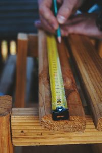 Cropped image of man measuring wooden plank with tape measure