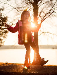 Full length of girl standing by lake against sky during sunset