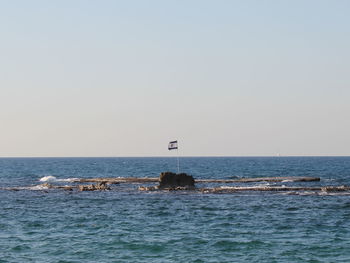 Israeli flag on rock in sea against sky