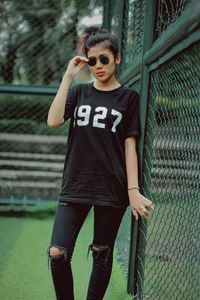Portrait of young man standing against chainlink fence