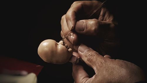 Cropped hands of craftsperson making doll in workshop