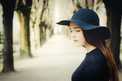 Beautiful young woman wearing hat while standing on pathway amidst trees