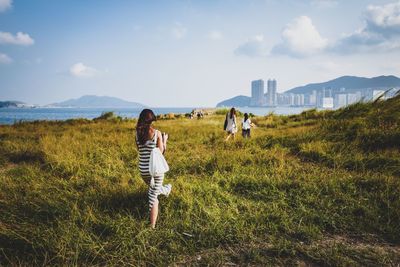 Friends walking on grassy landscape against sky