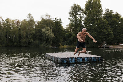 Senior man jumping from raft in a lake