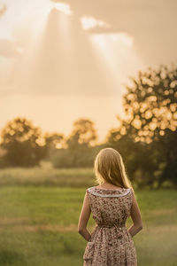 Rear view of woman standing on field against sky during sunset