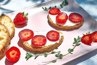 Toast bread with spread stracchino cheese and slices of ripe red strawberry on pink plate