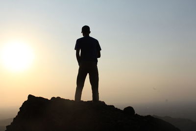 Rear view of silhouette man standing on rock against sky