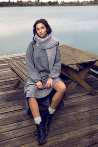 Woman sits next to the lake in a sweater and a scarf in the fall