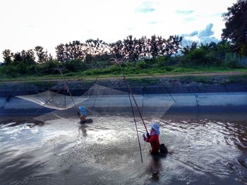 People fishing in water against sky