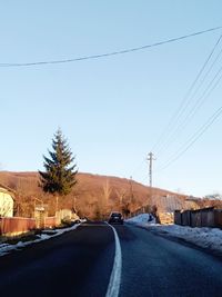 Road by electricity pylon against sky